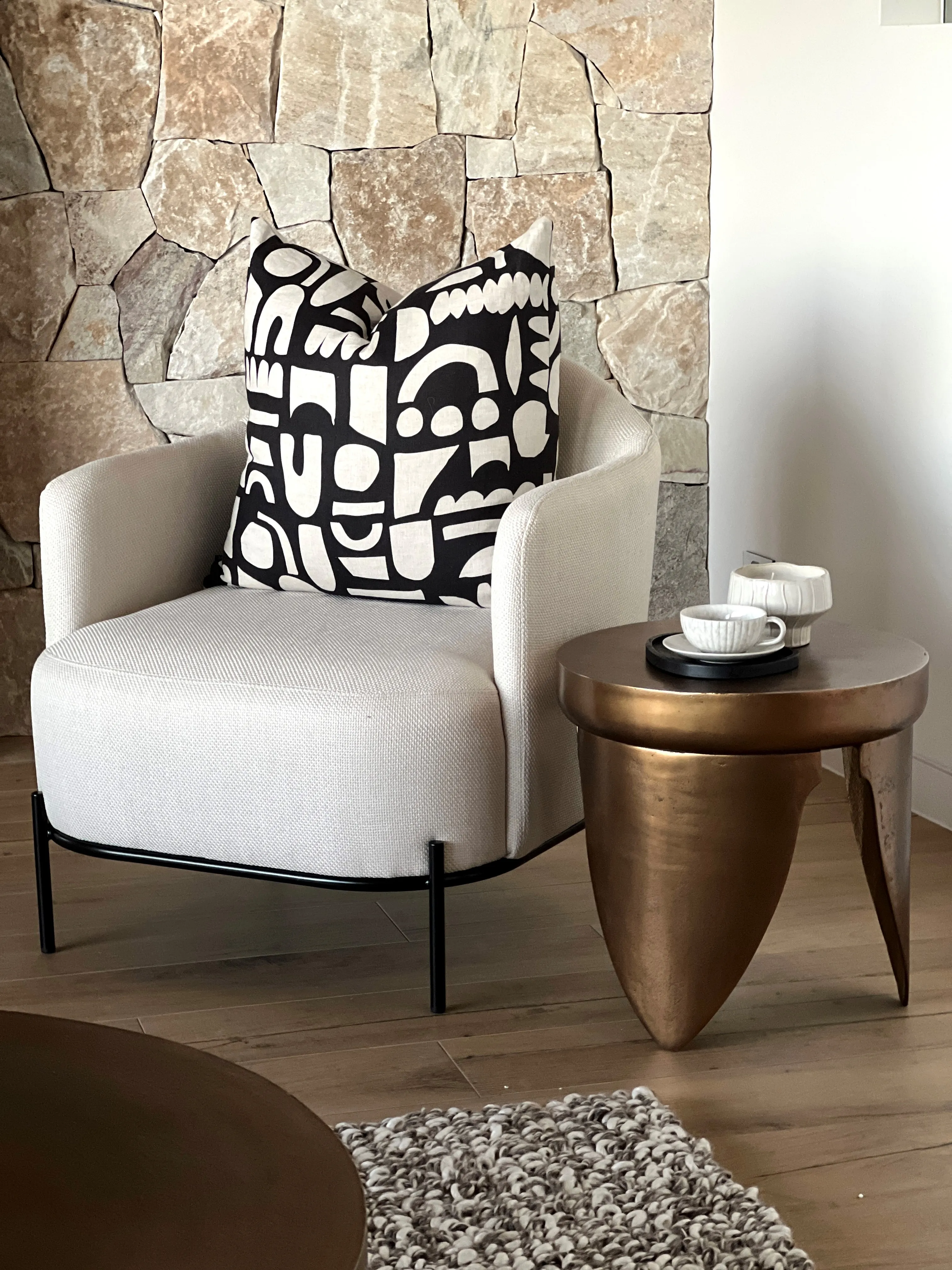 Cream armchair with abstract black cushion against sandstone feature wall and bronze side table